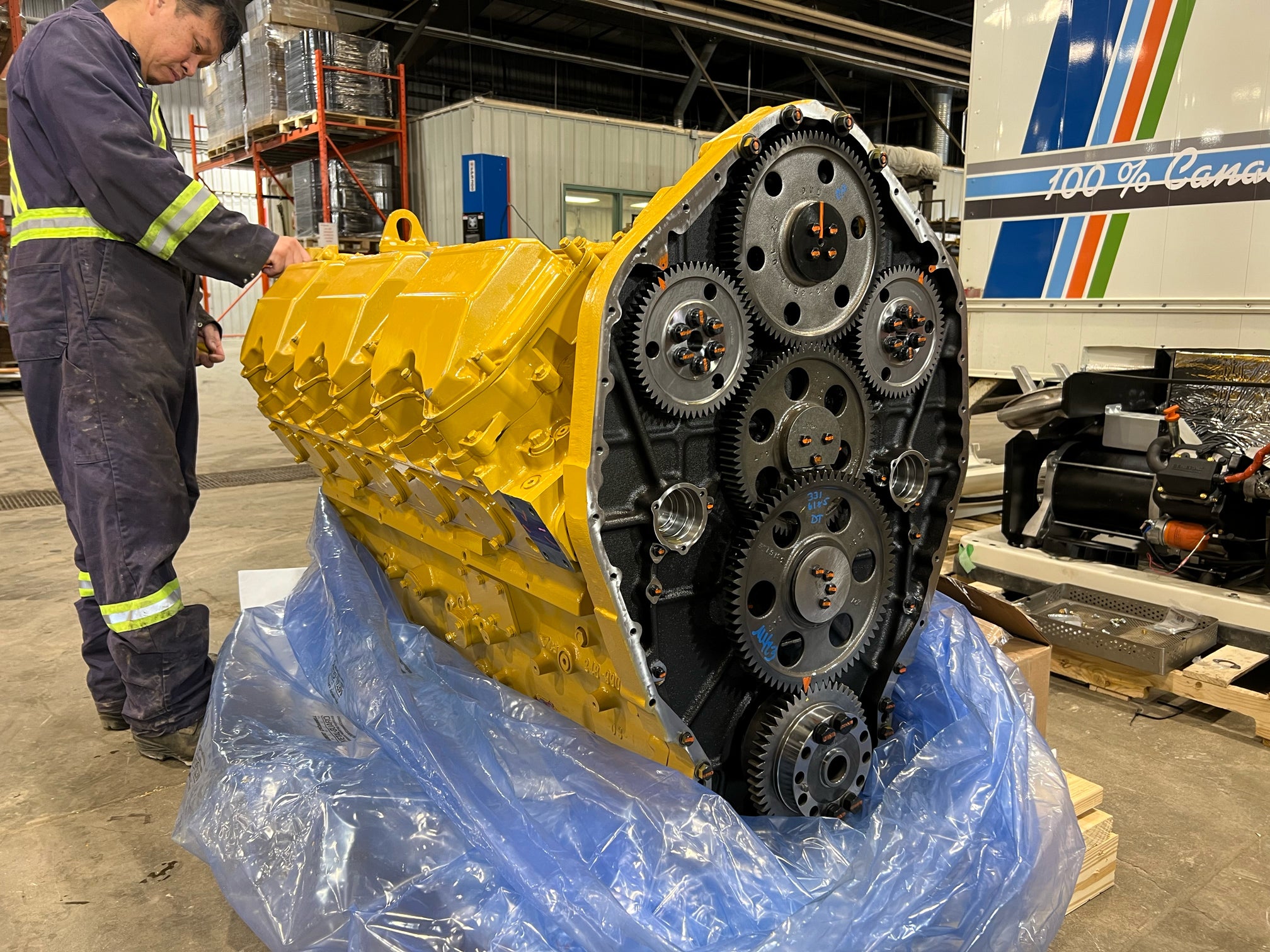 Large yellow and black mechanical component on a blue plastic sheet with a person inspecting it in an industrial setting.